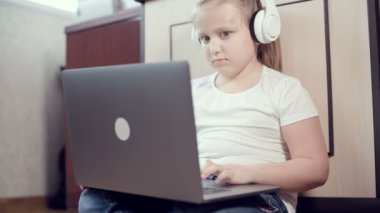 Yedi yaşında, elinde dizüstü bilgisayarla beyaz kulaklıklı akıllı bir kız odasında yere bastırıyor. İnternet ve bilişim teknolojisindeki genç nesil.