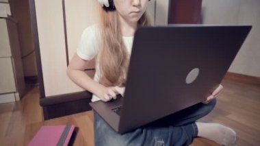 Yedi yaşında, elinde dizüstü bilgisayarla beyaz kulaklıklı akıllı bir kız odasında yere bastırıyor. İnternet ve bilişim teknolojisindeki genç nesil.