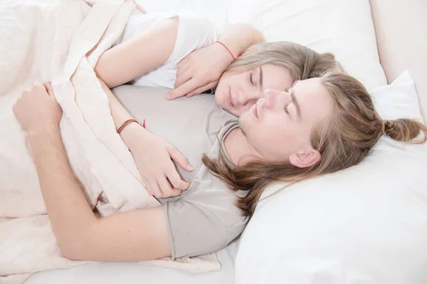 Primer plano de una joven pareja en la cama durmiendo en un abrazo, escondida detrás de una manta. El concepto de una familia joven y un sueño saludable — Foto de Stock