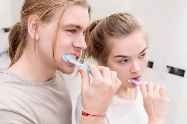 Young couple in bath brush teeth together, looking in mirror. Close-up