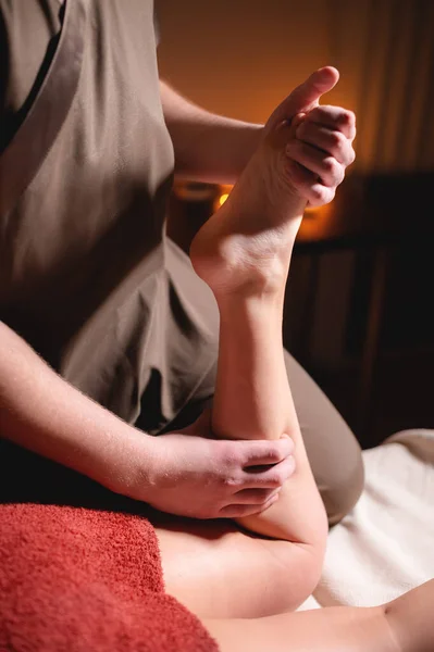 Premium samec luxusní masáž holeně anti-celulitida wellness komplex. Muž masér dělá masáž nohou na ženské klientce v kanceláři s tmavým světlem na pozadí hořících svíček — Stock fotografie