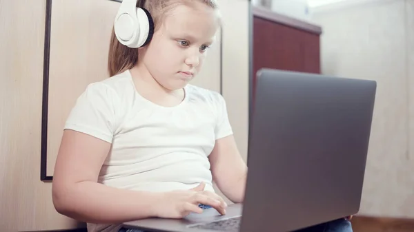 Elinde dizüstü bilgisayarla beyaz kulaklıklı akıllı küçük bir kız odasında yere bastırıyor. İnternet ve bilişim teknolojisindeki genç nesil. — Stok fotoğraf