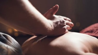 Close-up Young male massage therapist does back massage to a woman with a tattoo in a massage room with dim lights on the background of candles. Low key premium massage concept