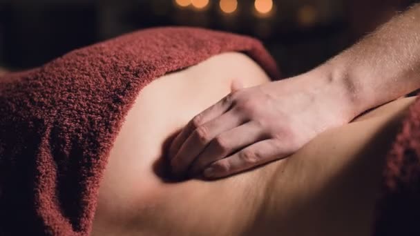 Крупным планом руки Профессиональный премиальный массаж в темном атмосферном шкафу. Молодой человек делает массаж клиентке женщины в темном кабинете на фоне горящих свечей — стоковое видео