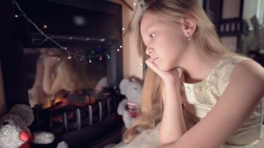 Küçük üzgün, hayal kırıklığına uğramış bir kız yapay bir şöminenin yanında oturur ve yumuşak oyuncakların yanında üzülür. Bozuk Noel tatili konsepti
