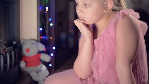 Маленька сумна розчарована дівчина сидить біля штучного каміна і сумна біля м'яких іграшок. Поняття зіпсованого різдвяного свята — стокове відео