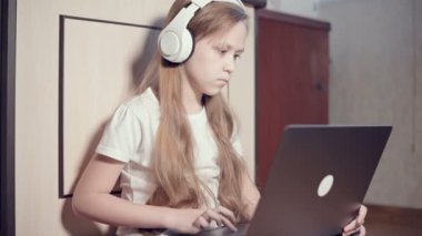 Yedi yaşında, elinde dizüstü bilgisayarla beyaz kulaklıklı akıllı bir kız odasında yere bastırıyor. İnternet ve bilişim teknolojisindeki genç nesil.