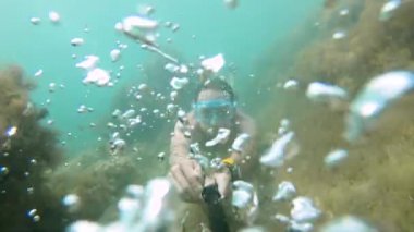 Maskeli kaslı adam suyun altında yüzüyor, elinde kamera var. Yakın plan..