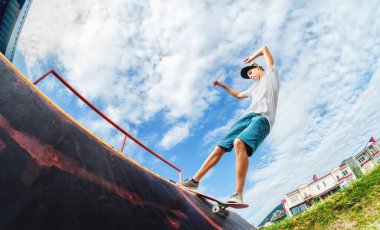 Güneşli bir günde yaz aylarında kaykay parkında kaykay pistinde kaykay yapan genç bir kaykaycının portresi. Gençlik eğlence ve spor kültürü kavramı.