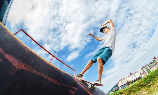 Portret van een jonge skateboarder die een truc uithaalt op zijn skateboard op een halfpipe helling in een skatepark in de zomer op een zonnige dag. Het begrip jongerencultuur van vrijetijdsbesteding en sport — Stockfoto