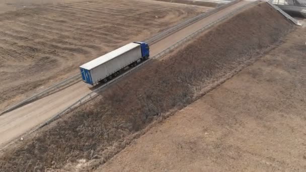 郊外の高速道路の近くにUターンのための場所を求めて未舗装道路に沿って運転トレーラー付き大型トラックの空中ビュー. — ストック動画