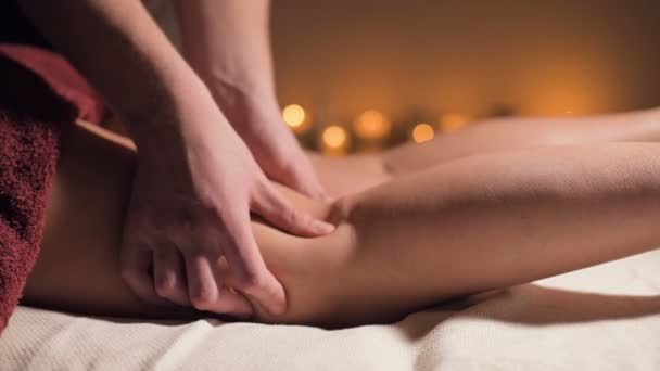 Primer plano del masaje premium anti-celulitis en el muslo. Las manos masculinas hacen masaje de bienestar del muslo a la niña paciente en un acogedor estudio con poca luz. Servicios de masajes de lujo — Vídeo de stock