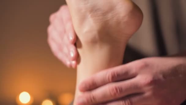 Close-up Fisioterapeuta profesional masajista masculino en una oficina con acogedora iluminación oscura hace un masaje de pies wellness a una clienta femenina. Masaje terapéutico para pies y piernas — Vídeo de stock