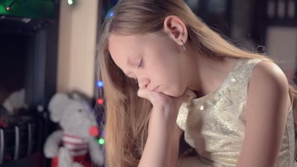 A little sad disappointed girl sits by an artificial fireplace and is sad next to soft toys. The concept of spoiled Christmas holiday — Stock Video