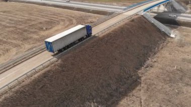 Bir banliyö otoyolunun yakınlarında U dönüşü yapmak için toprak bir yol boyunca giden büyük bir kamyonun hava görüntüsü..