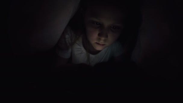 Uma menina está se escondendo sob um cobertor para usar um dispositivo de smartphone tablet digital tarde após o sono. Solidão de crianças pequenas e resgate pelo telefone . — Vídeo de Stock