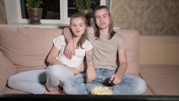 Young cute couple sitting hugging in living room, watching TV, eating popcorn. — Stock Video