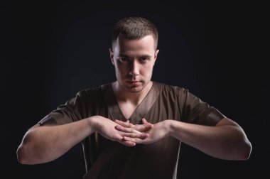 Stüdyoda güçlü ve genç bir manuel terapistin portresi ve zıt ışık altında masaj terapisti. Masör, masajdan önce yüzünde hafif bir sırıtışla ellerini ustalaştırır.