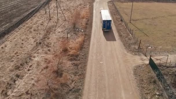 Vista aérea de um grande caminhão com um reboque dirigindo ao longo de uma estrada de terra em busca de um lugar para um U-turn nas proximidades de uma estrada suburbana. — Vídeo de Stock