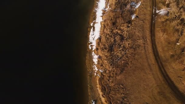 Bovenaanzicht vanuit de lucht op een warme winterdag. Gele gras en stukken sneeuw op de kust. Opwarmingsconcept. Voorwaartse beweging — Stockvideo