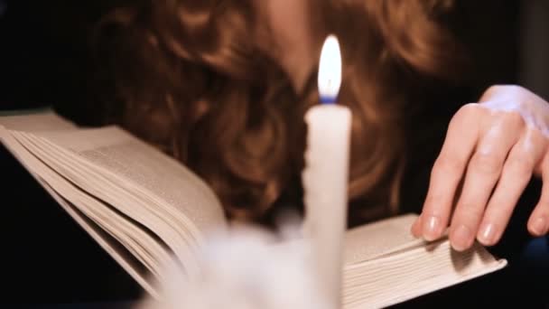 衣服吸引人的高加索女孩翻阅一本书。蜡烛在燃烧。万圣节庆祝的概念。浅水区深度 — 图库视频影像