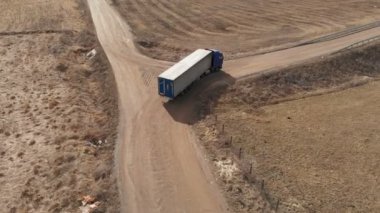 Bir banliyö otoyolunun yakınlarında U dönüşü yapmak için toprak bir yol boyunca giden büyük bir kamyonun hava görüntüsü..