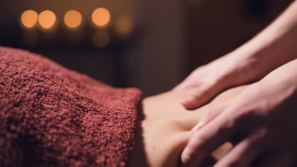 Close-up Jonge mannelijke massage therapeut doet rug massage aan een vrouw met een tatoeage in een massageruimte met schemerige lichten op de achtergrond van kaarsen. Low-key premium massageconcept — Stockvideo