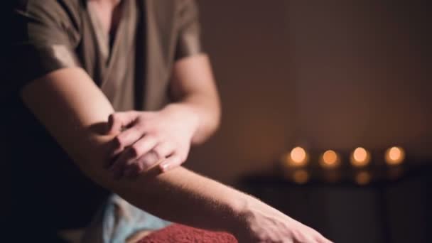 Мужская рука профессионального физиотерапевта-массажиста, делающего поясничный массаж пациентке женского пола в роскошной массажной комнате с тусклым светом — стоковое видео