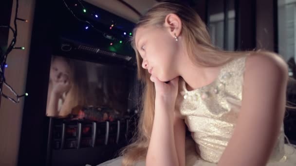 Trochę smutna rozczarowana dziewczyna siedzi przy sztucznym kominku i jest smutna obok miękkich zabawek. Koncepcja zepsutych świąt Bożego Narodzenia — Wideo stockowe