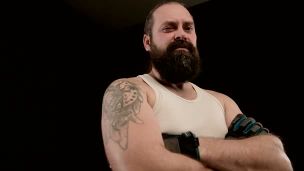 A szakállas férfi fekete háttérrel keresztbe teszi a karját, dühöt sugároz. Közelkép — Stock videók
