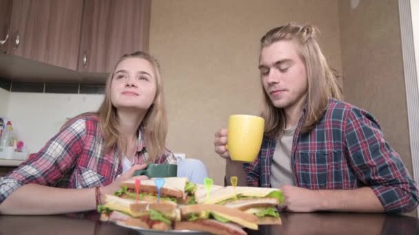 Young couple sitting in kitchen, drinking from cups, chatting. Closeup — Stock Video