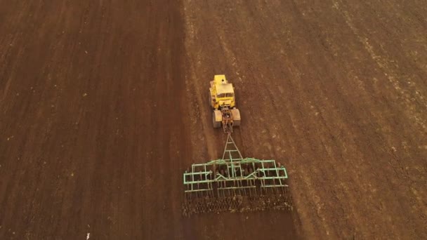 Luftaufnahme eines leistungsstarken gelben Traktors mit großem Aufwand am Haken, der die Bodenbearbeitung für die Aussaat von Wintergetreide mit einem Scheibenmulchgerät im Herbst durchführt — Stockvideo