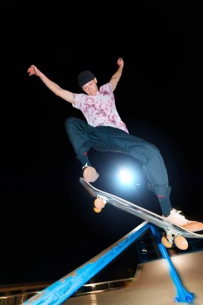 Een jonge schaatser 's nachts in een skatepark doet de truc op de reling. Röntgencultuur nachtleven concept — Stockfoto
