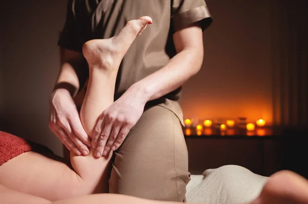 Premium mannelijke luxe shin massage anti-cellulitis wellness complex. man masseur doen been massage naar een vrouwelijke client in een kantoor met donker licht op een achtergrond van brandende kaarsen — Stockfoto