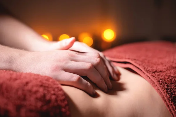 Closeup of the massage therapist physiotherapists hand on the stomach of a woman client in a massage parlor. The concept of healing and professional massage of the abdomen — Stock Photo, Image