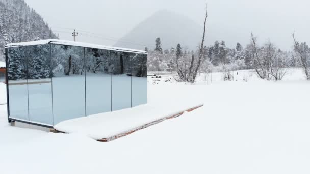 Luchtfoto van een innovatief hightech huis met spiegelende transparante muren in de winter in de buurt van een naaldbos in de bergen van de Kaukasus of de Alpen. — Stockvideo