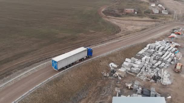 Vue aérienne d'un grand camion avec une remorque roulant le long d'un chemin de terre à la recherche d'un endroit pour un demi-tour à proximité d'une autoroute de banlieue. — Video