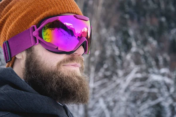 Portrait of a bearded male athlete in an orange knitted hat and ski mask on a background of a snowy forest. Winter sports concept — Stock Photo, Image