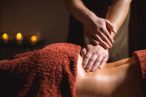Close-up male hand of a professional physiotherapist masseur doing lumbar massage to a female patient in a massage luxury room with dim light — Stock Photo, Image