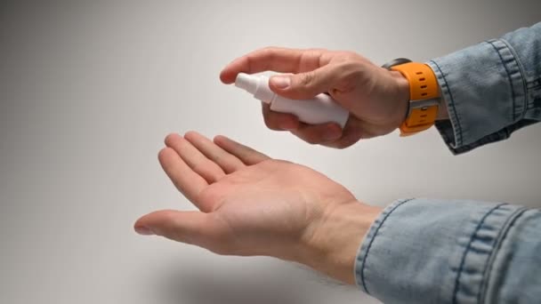 黄色のストラップと手のひらの表面を治療するために消毒剤をスプレーし、親指を上げるジェスチャーを示す消毒剤を使用して時計と青のデニムシャツのクローズアップ男性の手. — ストック動画