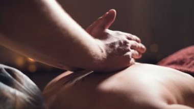 Close-up Young male massage therapist does back massage to a woman with a tattoo in a massage room with dim lights on the background of candles. Low key premium massage concept