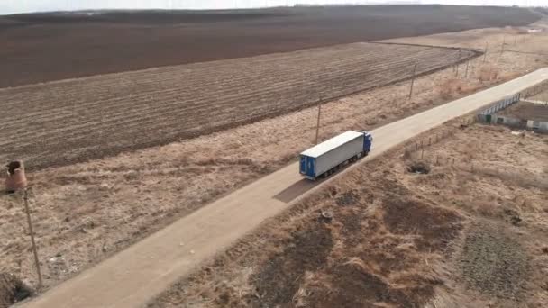 Vista aérea de un camión grande con un remolque que conduce a lo largo de un camino de tierra en busca de un lugar para un giro en U en las inmediaciones de una carretera suburbana. — Vídeo de stock