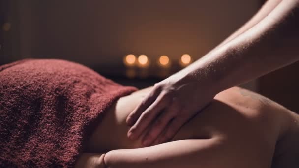 Крупный план Молодой массажист-мужчина делает массаж спины женщине с татуировкой в массажной комнате с тусклыми лампами на фоне свечей. Низкий ключ премиум массаж — стоковое видео
