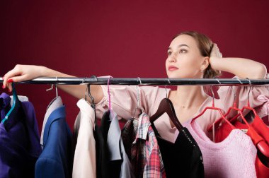 Askıda asılı duran şeylerin arasında kırmızı arka planda duran çekici bir kızın portresi. Giyecek bir şey yok. Ne giyeceğine kadın karar verir. Moda tarzı