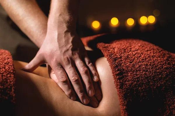Primer plano mano masculina de un masajista fisioterapeuta profesional haciendo masaje lumbar a una paciente femenina en una habitación de lujo de masaje con poca luz — Foto de Stock
