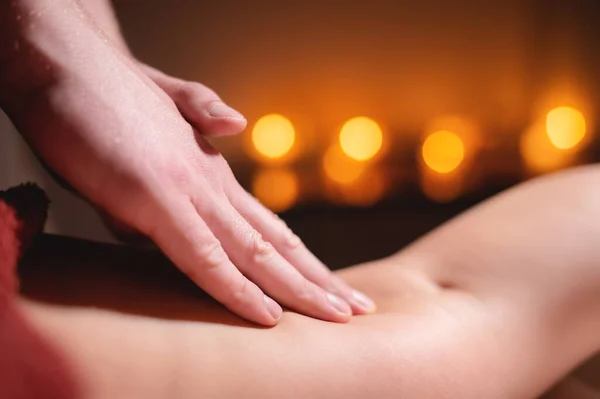 Close-up low key on womans thigh massage in a professional premium spa salon, man masseur does in a dark room on the background of burning candles — Stock Photo, Image