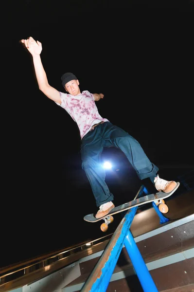 Un giovane pattinatore di notte in uno skatepark fa il trucco sulla ringhiera. Cultura a raggi X concetto di vita notturna — Foto Stock