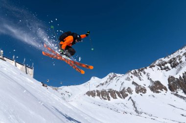 Turuncu tetik kullanan erkek bir kayakçı, Kuzey Kafkasya 'daki Elbrus Dağı' nın arka planında uçan kar tozuyla sıçrama yapıyor. Kış Ekstrem Spor Konsepti
