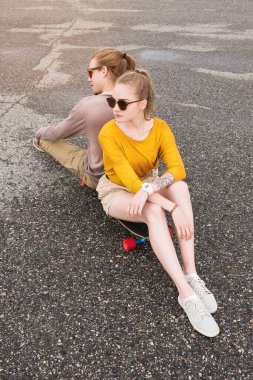 Çekici, uzun saçlı bir çiftin portresi sırt sırta oturup asfalt bir banliyö otoparkında dinleniyor. Tarz ve gençlik kültürü. Mutlu çift