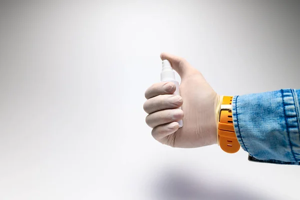 Una mano masculina en un guante blanco de goma y una camisa de mezclilla sostiene la aplicación de un aerosol desinfectante contra los virus. Concepto para el uso exitoso de agentes antivirales durante una pandemia — Foto de Stock